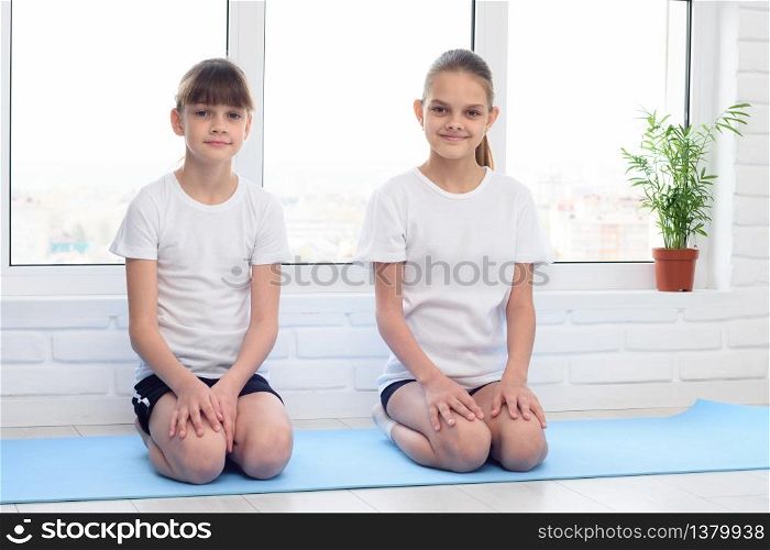 Two sisters are sitting at home on a sports mat before training
