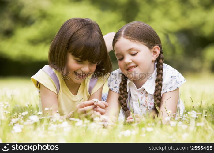 Two sisters lying outdoors with flower smiling