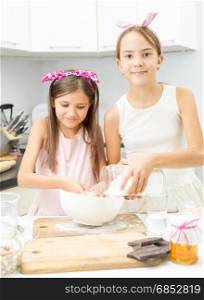 Two sisters making dough on kitchen in big white bowl