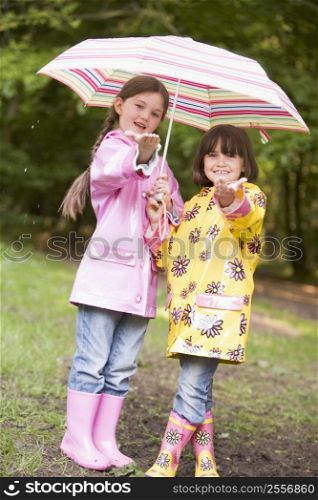Two sisters outdoors in rain with umbrella smiling