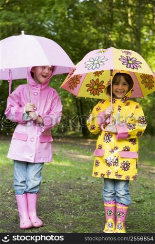 Two sisters outdoors in rain with umbrellas smiling