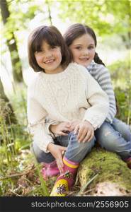 Two sisters outdoors in woods sitting on log smiling