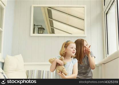 Two sisters pointing and looking out of holiday apartment window