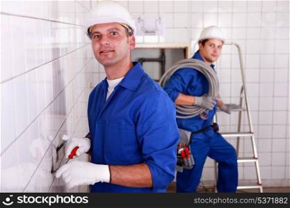 two skilled tradesman in blue jumpsuites working in a empty room