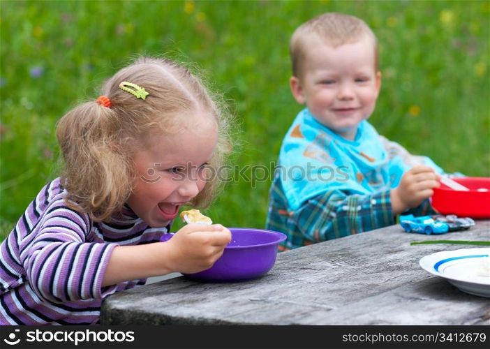Two small children eating at the table outdoors