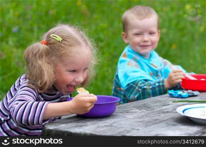 Two small children eating at the table outdoors