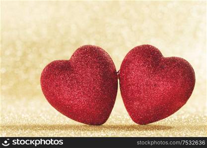 Two small handmade red glitter hearts on bright golden lights bokeh background Valentines day card. Two hearts on bokeh background