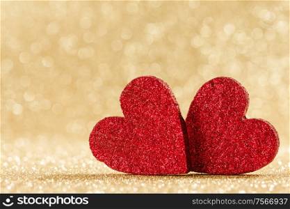 Two small handmade red glitter hearts on bright golden lights bokeh background Valentines day card. Two hearts on bokeh background