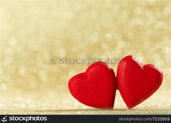 Two small handmade red wooden hearts on bright golden lights bokeh background Valentines day card. Two hearts on bokeh background