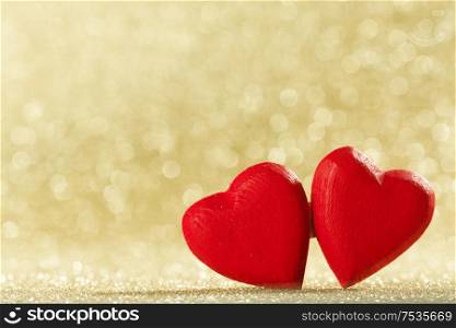 Two small handmade red wooden hearts on bright golden lights bokeh background Valentines day card. Two hearts on bokeh background