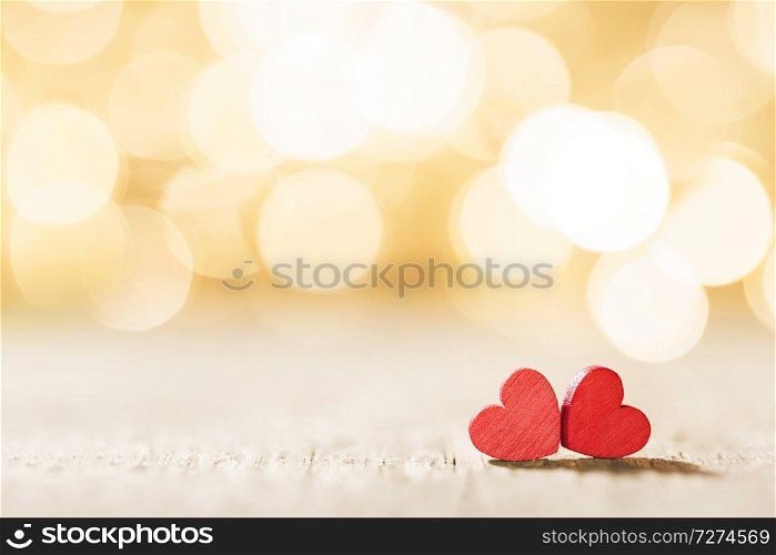 Two small handmade red wooden hearts on golden bright lights bokeh background. Red hearts on bokeh background