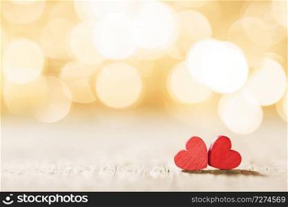 Two small handmade red wooden hearts on golden bright lights bokeh background. Red hearts on bokeh background