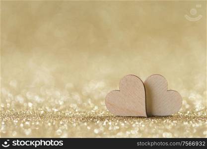 Two small handmade wooden hearts on bright golden lights bokeh background Valentines day card. Two hearts on bokeh background