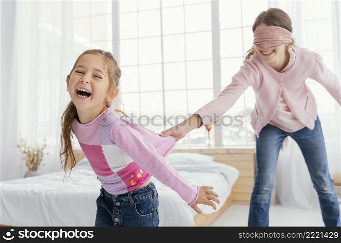 two smiley sisters playing home while blindfolded