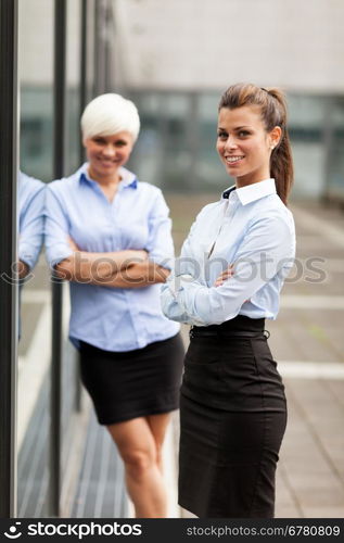 Two smiling and successful businesswoman next to a glass wall