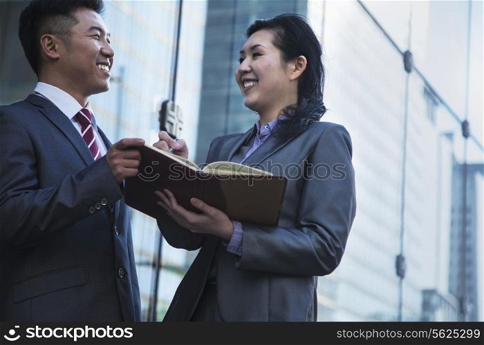 Two smiling business people outside meeting and writing in personal organizer