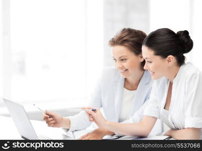 two smiling businesswomen working with laptop in office