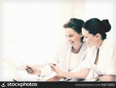two smiling businesswomen working with laptop in office
