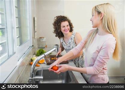 two smiling female friends working kitchen looking each other