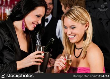 Two smiling girl friends enjoy glass of champagne at bar