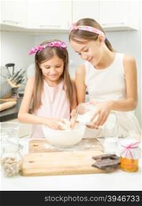 Two smiling girl making dough in white bowl on kitchen
