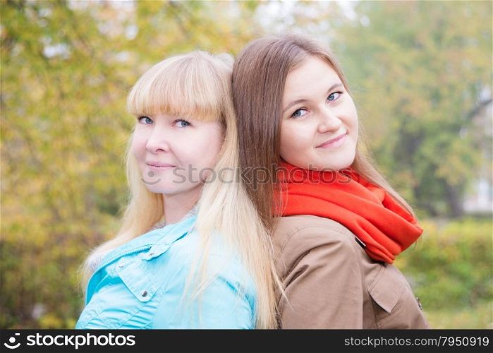 Two smiling girls are in autumn park at foggy morning