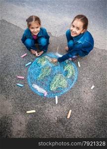 Two smiling girls drawing Earth with chalks on street
