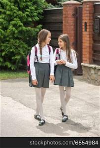 Two smiling girls in uniform walking to school and chatting