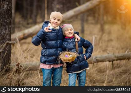 Two smiling girls posing with basket full of Easter eggs at forest