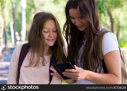 two smiling girls students with the tablets outdoors