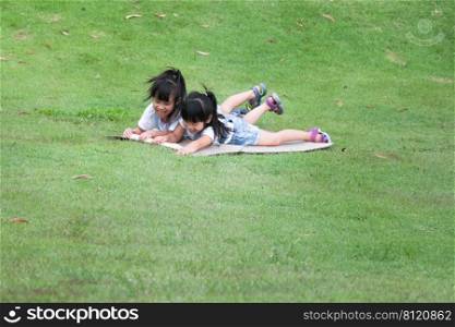 Two smiling little sisters lie prone on cardboard boxes sliding down the hill at the Botanical Gardens. The famous outdoor learning center of Mae Moh Mine Park, L&ang, Thailand. Happy childhood conc