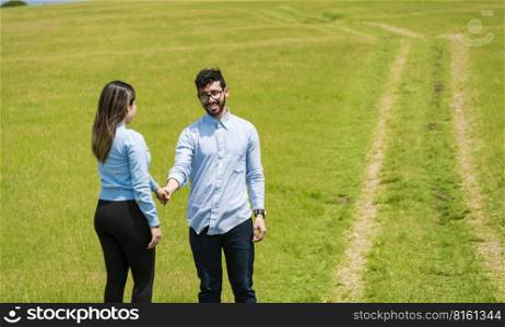 two smiling lovers in the field holding hands, Beautiful couple holding hands looking at each other in the field, two persons holding hands in the field