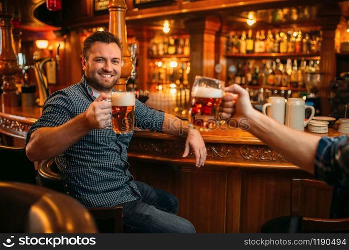 Two smiling male friends drinks beer at the counter in pub. Bearded men with mugs having fun in bar, good friendship. Two male friends drinks beer at the counter in pub