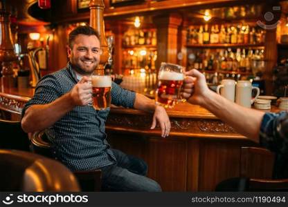 Two smiling male friends drinks beer at the counter in pub. Bearded men with mugs having fun in bar, good friendship. Two male friends drinks beer at the counter in pub