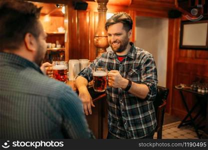 Two smiling male friends drinks beer at the counter in pub. Bearded men with mugs having fun in bar, good friends. Two male friends drinks beer at the counter in pub