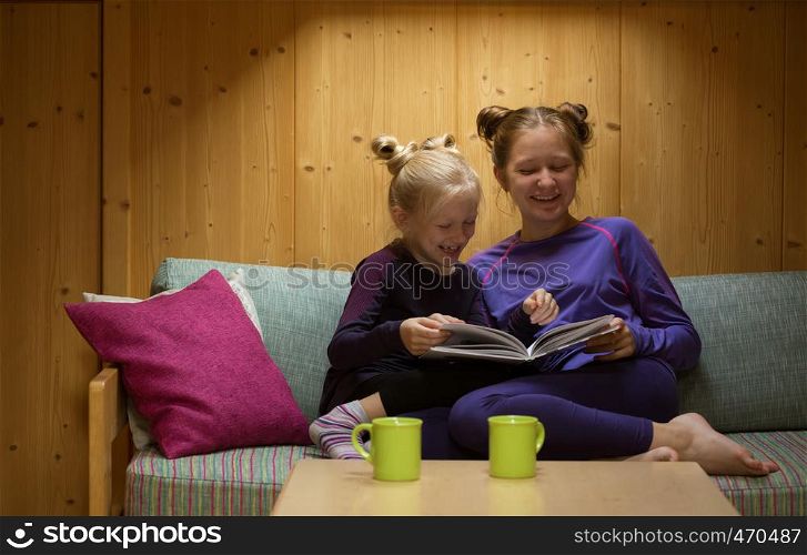 two smiling sisters girls reads book in your room