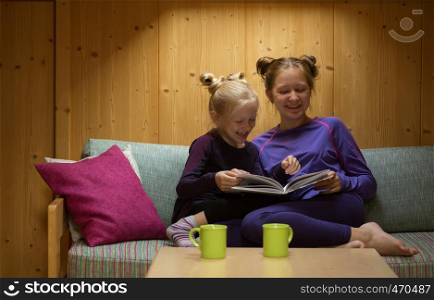 two smiling sisters girls reads book in your room
