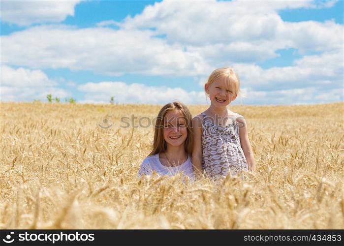 two smiling sisters sitting at the wheat field