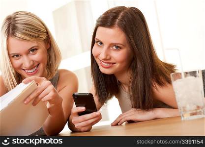 Two smiling students enjoying free time with book and mobile phone