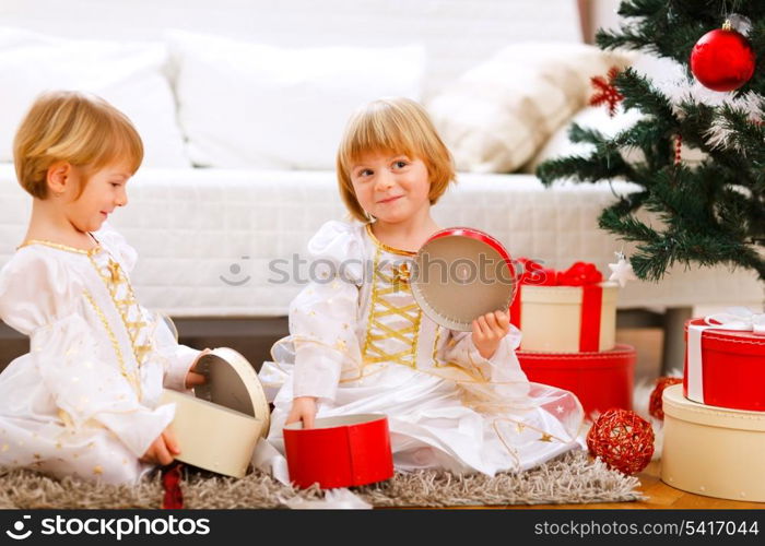 Two smiling twins girl opening presents near Christmas tree&#xA;