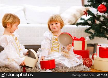 Two smiling twins girl opening presents near Christmas tree&#xA;