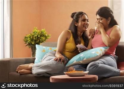 Two smiling women using mobile phone together while relaxing on sofa in living room