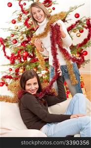 Two smiling women with Christmas chains decorating tree