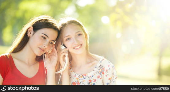 Two Smiling Young Girls with Pleasure Listening to Music on Headphones on a fine Summer Day