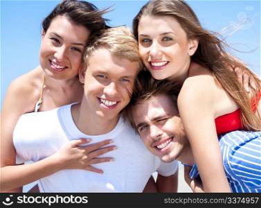 Two Smiling Young man giving piggyback to their girlfriends on holiday. Girls hugging there boyfriend