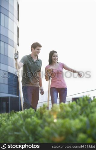 Two smiling young people gardening and pointing at plants in a roof top garden in the city