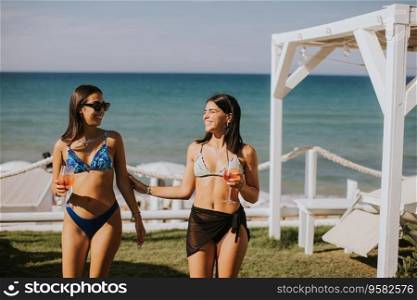 Two smiling young women in bikini enjoying vacation on the beach while drinking cocktail