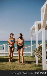 Two smiling young women in bikini enjoying vacation on the beach while drinking cocktail