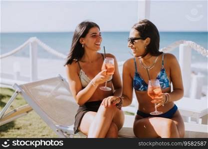 Two smiling young women in bikini enjoying vacation on the beach while drinking cocktail