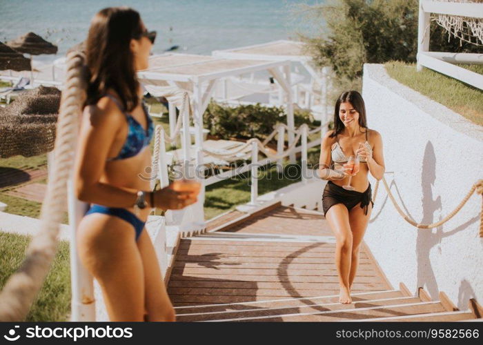 Two smiling young women in bikini enjoying vacation on the beachwhile drinking cocktail